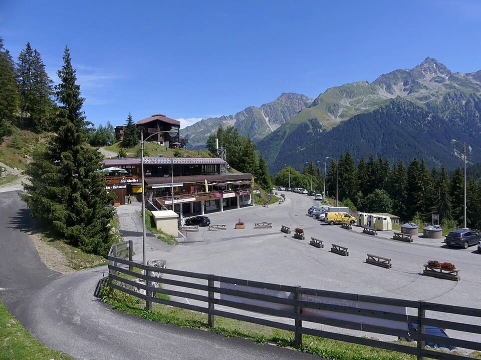 A wide, landscape view of Le Pleynet village in summer, surrounded by the green peaks of the Belledonne massif, clear sky